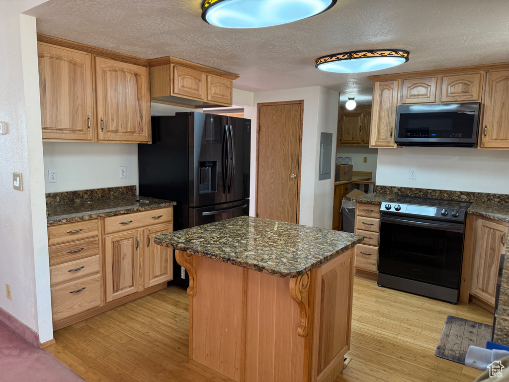 Kitchen featuring black appliances, light wood finished floors, dark stone counters, a center island, and a textured ceiling