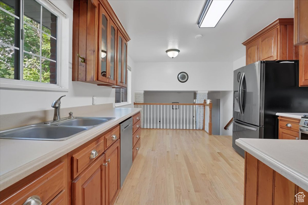 Kitchen featuring stainless steel appliances, light countertops, light wood finished floors, brown cabinets, and glass insert cabinets