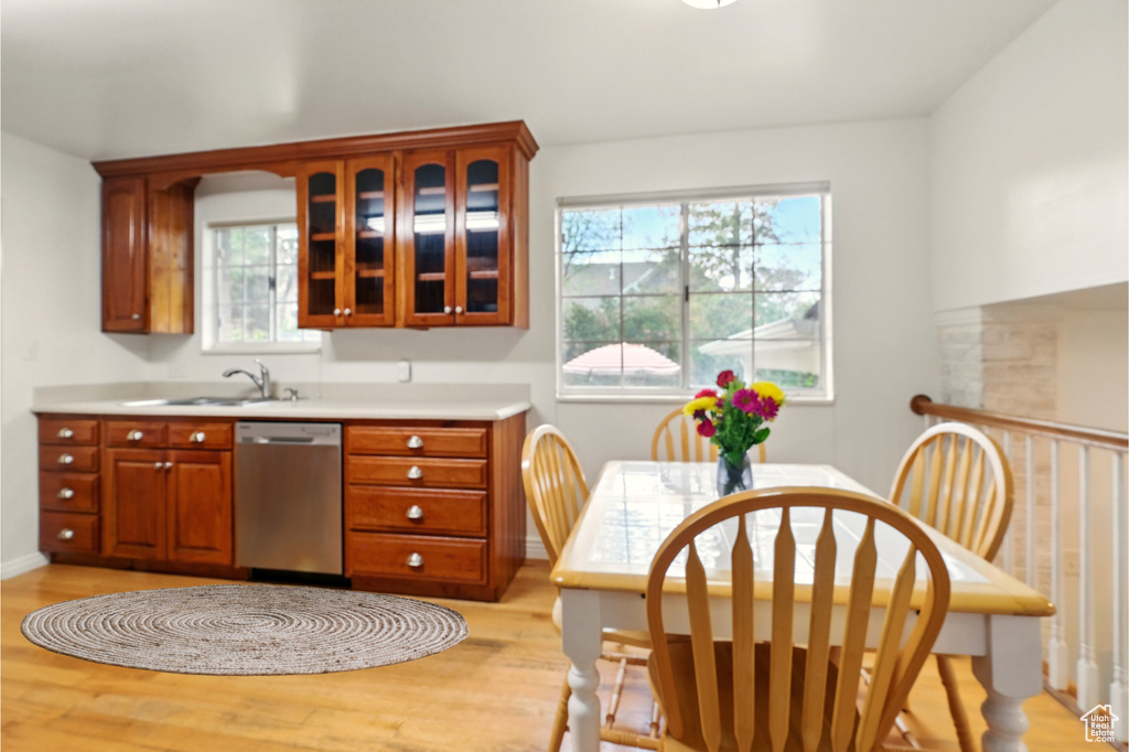Kitchen featuring stainless steel dishwasher, light wood-style floors, a sink, glass insert cabinets, and light countertops