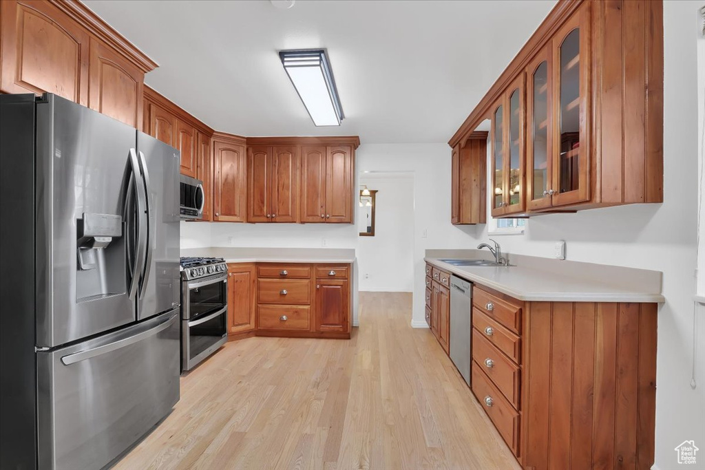 Kitchen featuring appliances with stainless steel finishes, light wood finished floors, brown cabinets, glass insert cabinets, and light countertops