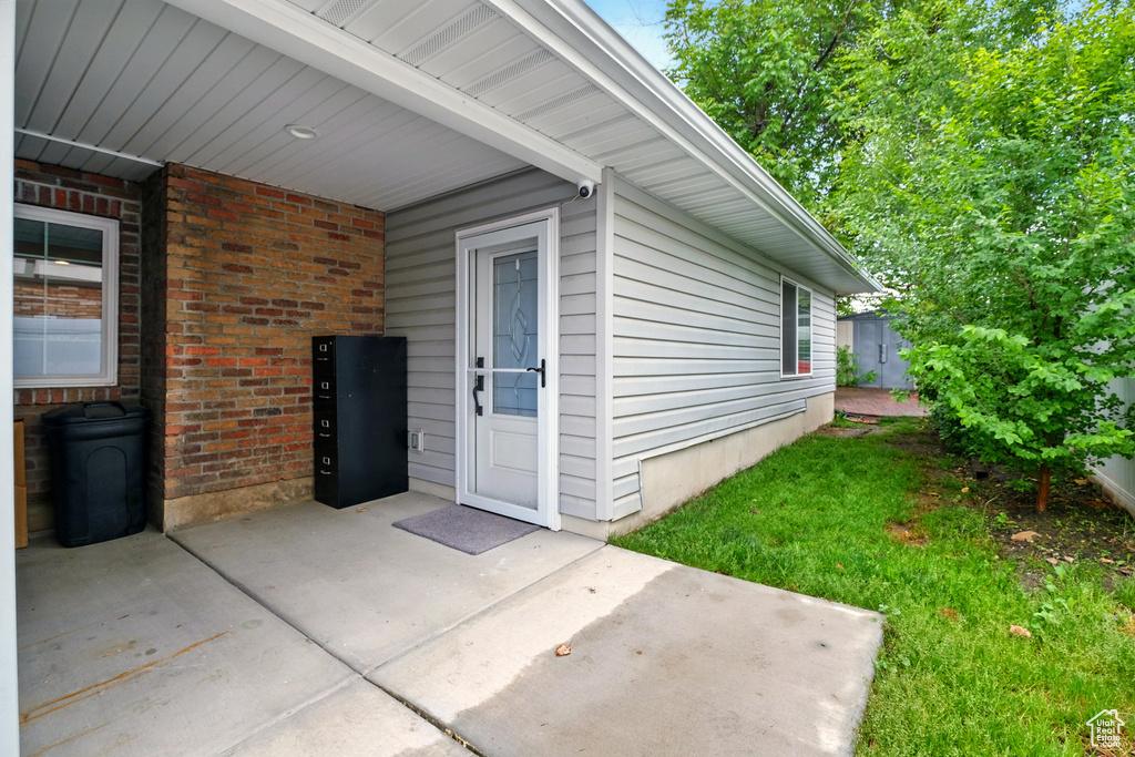 View of exterior entry featuring brick siding, a patio area, and a lawn
