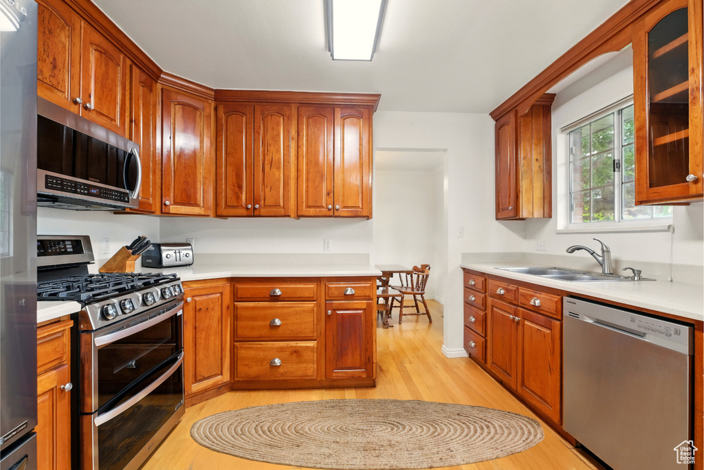 Kitchen with appliances with stainless steel finishes, a sink, light wood finished floors, and light countertops