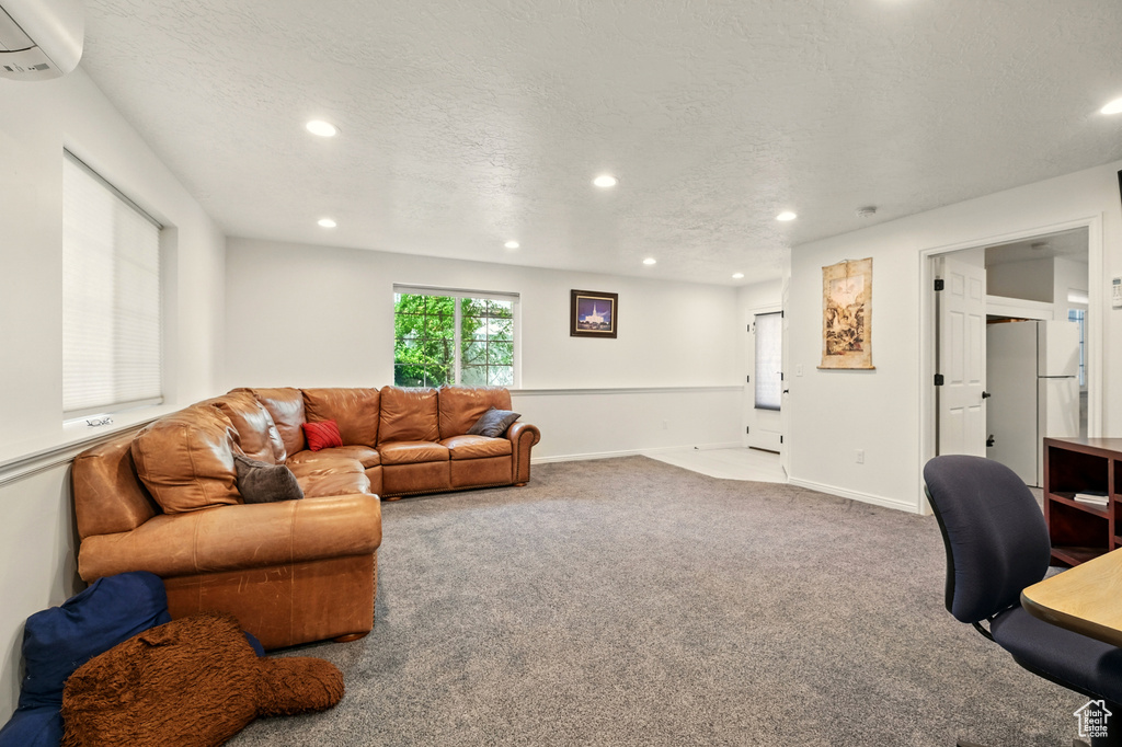 Carpeted living area featuring a wall mounted AC, recessed lighting, baseboards, and a textured ceiling
