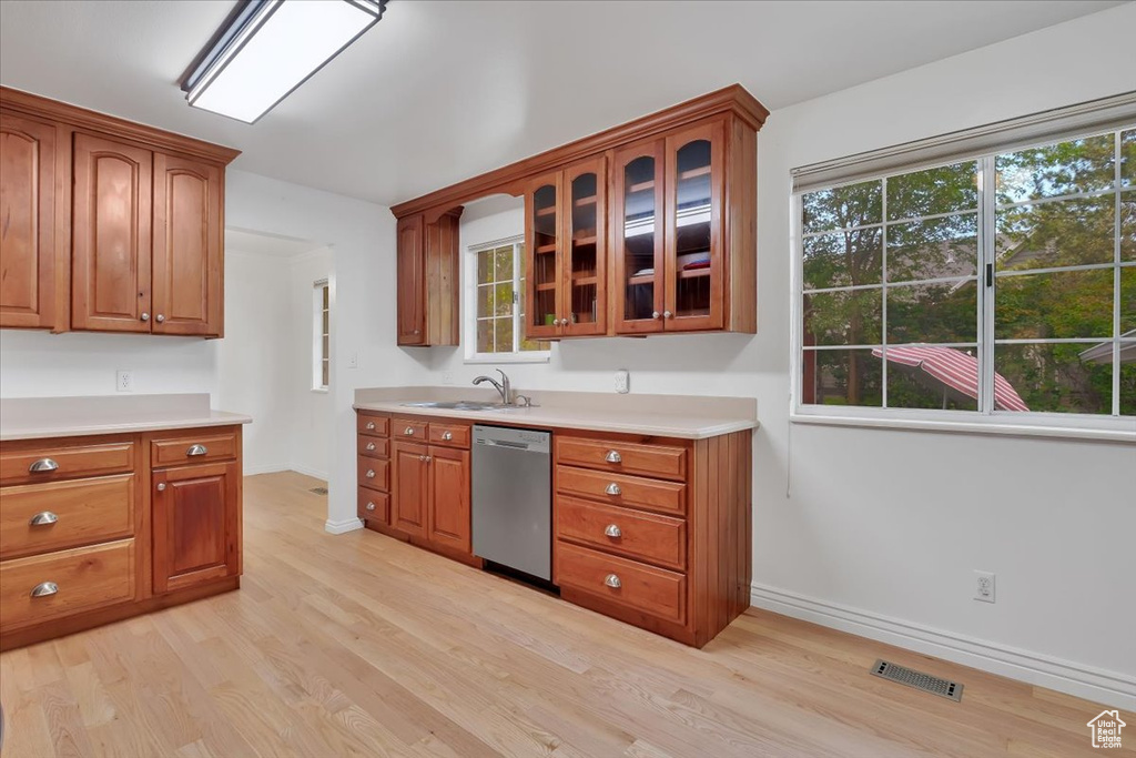Kitchen featuring dishwasher, light wood finished floors, light countertops, brown cabinetry, and glass insert cabinets