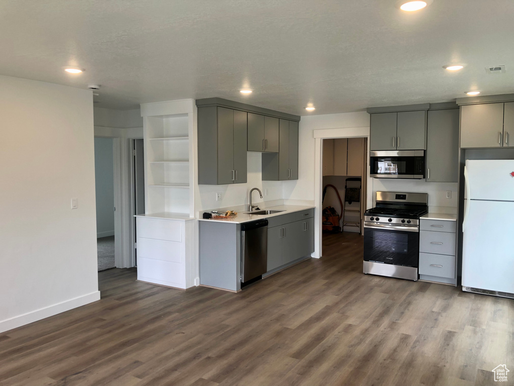 Kitchen featuring appliances with stainless steel finishes, a sink, gray cabinetry, dark wood-style flooring, and light countertops