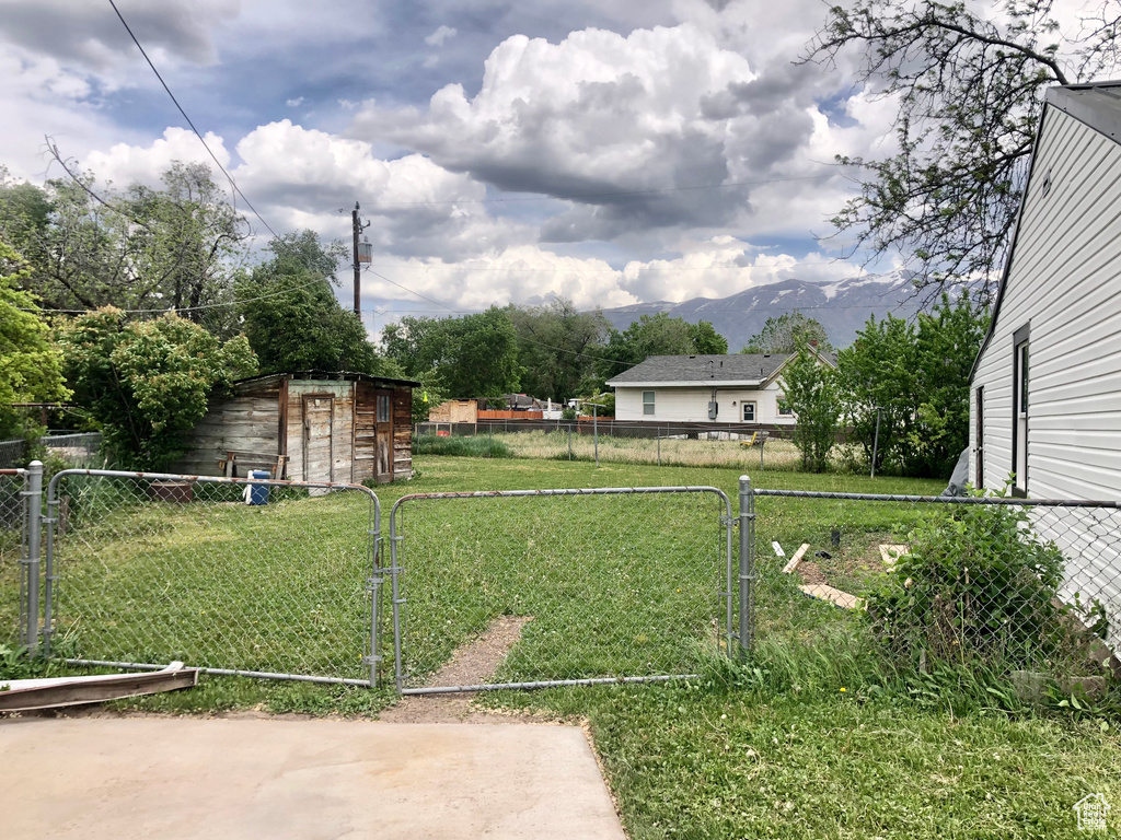 View of yard featuring a gate, a mountain view, a storage unit, and an outbuilding