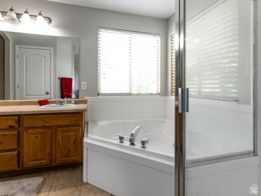 Full bathroom featuring double vanity, plenty of natural light, a garden tub, and tile patterned floors