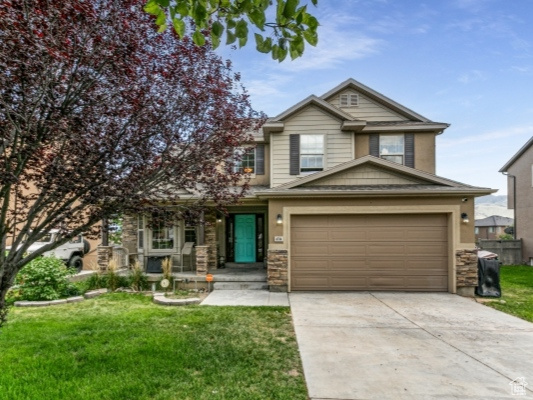 View of front facade featuring driveway, stone siding, a front lawn, and an attached garage