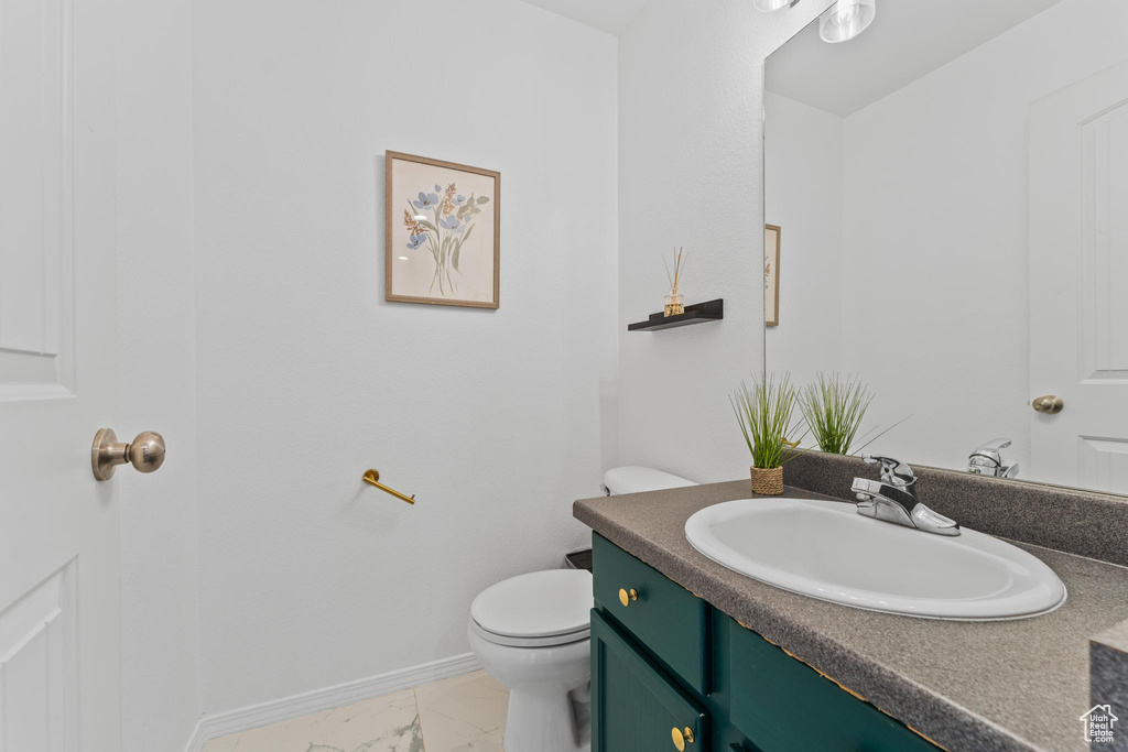 Bathroom with marble look tile flooring, baseboards, vanity, and toilet