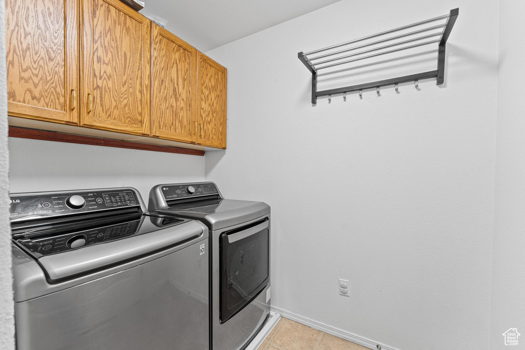 Laundry area featuring cabinet space, washing machine and clothes dryer, baseboards, and light tile patterned flooring
