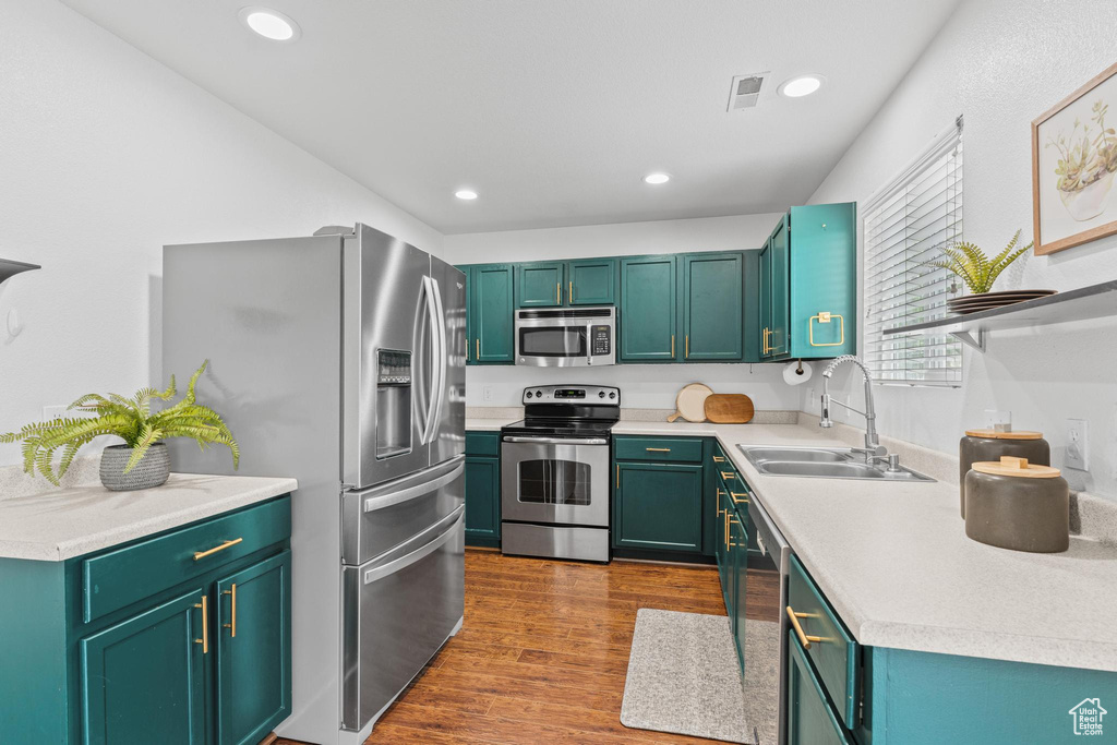 Kitchen with stainless steel appliances, a sink, light countertops, recessed lighting, and dark wood-type flooring