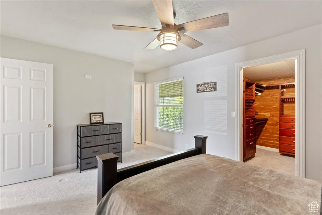 Bedroom with light carpet, a walk in closet, baseboards, and ceiling fan