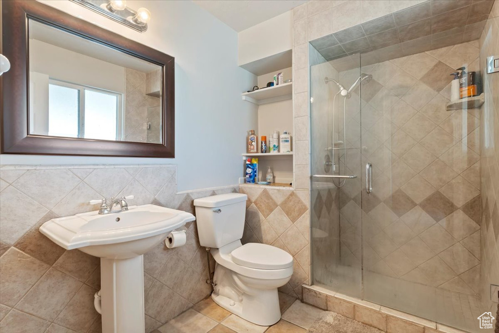 Full bathroom with tile walls, a shower stall, toilet, wainscoting, and tile patterned floors
