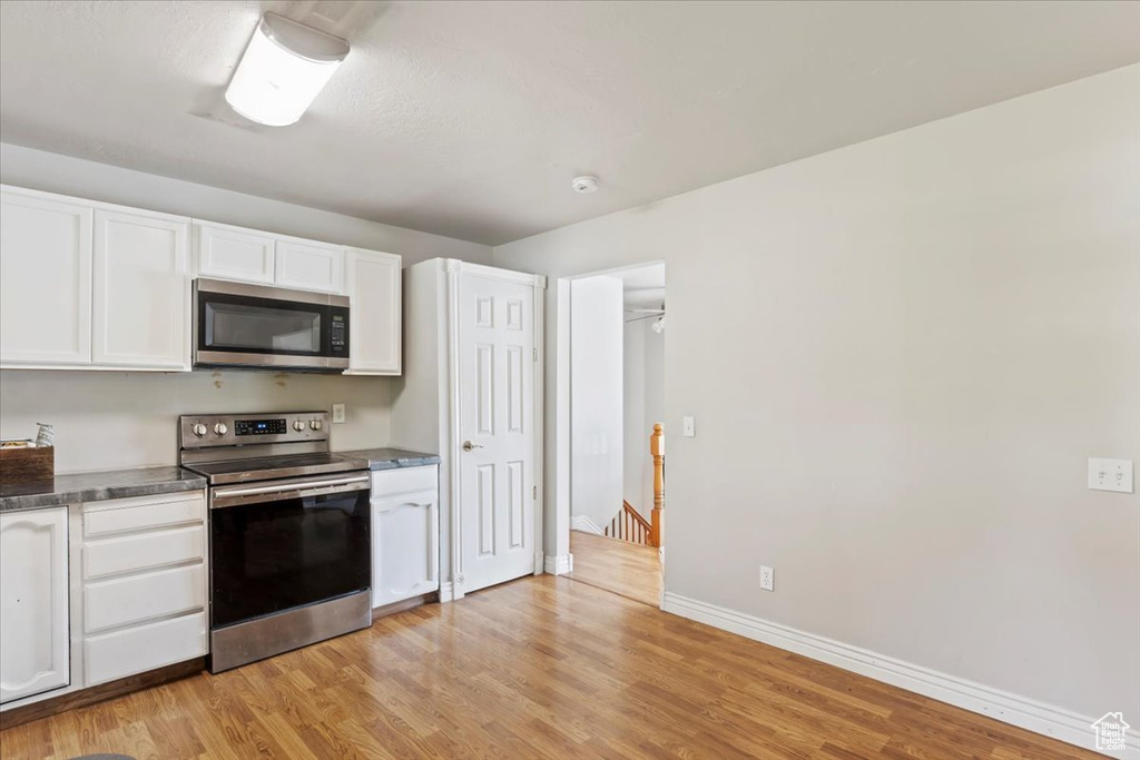 Kitchen featuring appliances with stainless steel finishes, light wood-style floors, white cabinetry, and baseboards