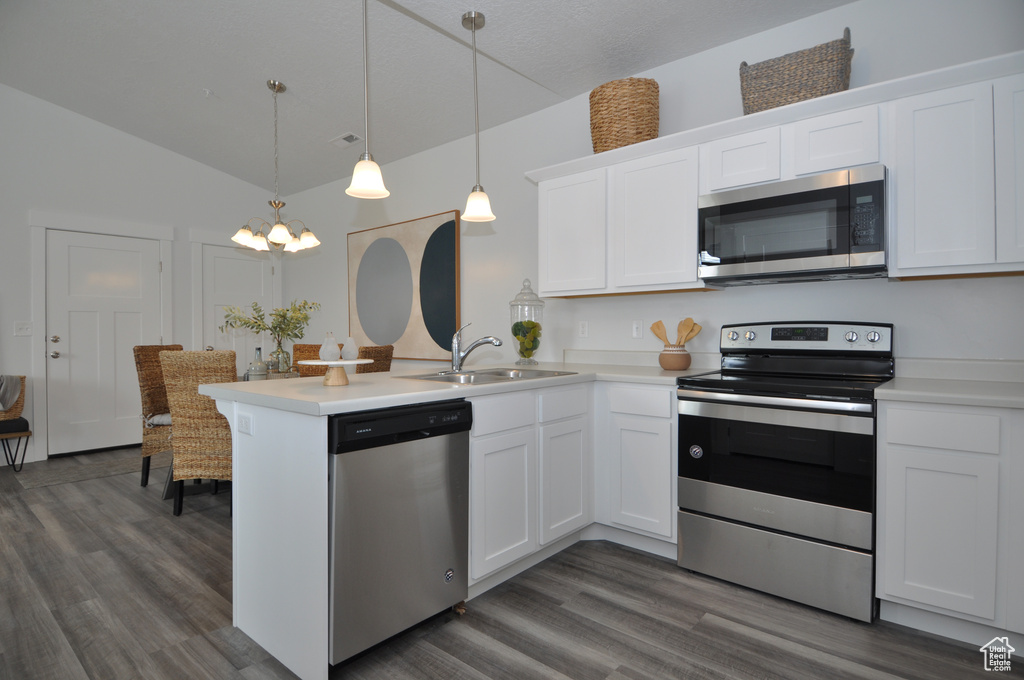 Kitchen featuring stainless steel appliances, a sink, a peninsula, vaulted ceiling, and dark wood-style flooring