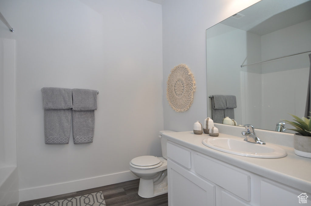 Full bath featuring wood finished floors, toilet, vanity, baseboards, and a shower