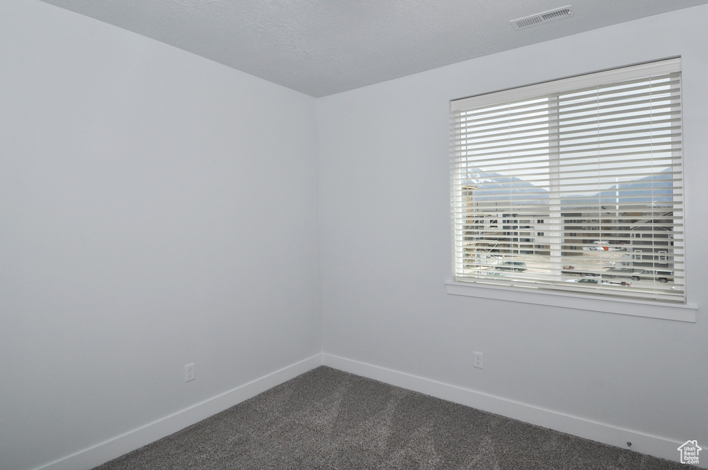 Unfurnished room with dark colored carpet, baseboards, and healthy amount of natural light