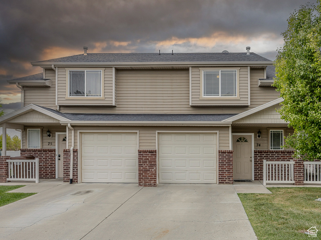 Multi unit property with brick siding, a porch, driveway, a garage, and a yard