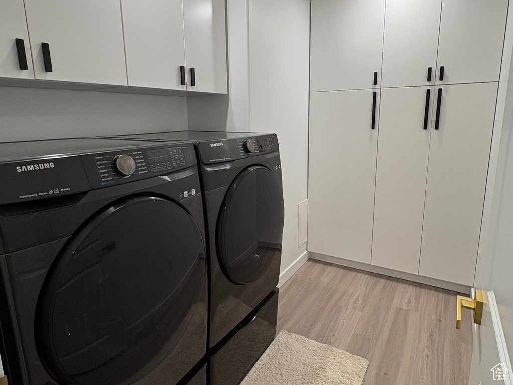 Washroom featuring cabinet space, washing machine and clothes dryer, light wood-type flooring, and baseboards