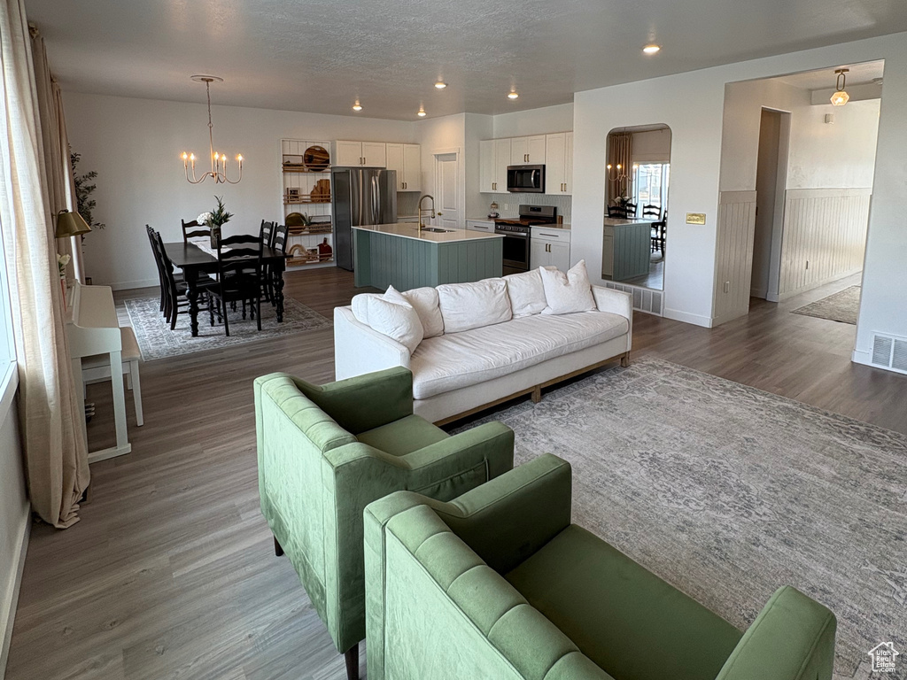 Living room with recessed lighting, light wood-type flooring, a chandelier, baseboards, and a textured ceiling