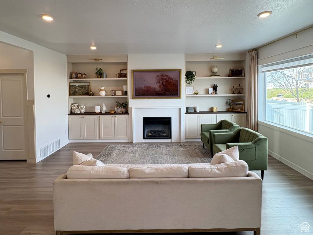 Living room featuring a textured ceiling, wood finished floors, baseboards, a fireplace, and recessed lighting