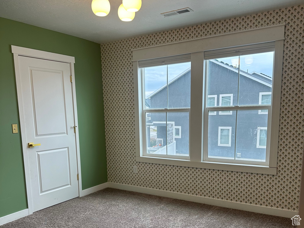 Spare room with wallpapered walls, a textured ceiling, carpet flooring, baseboards, and a chandelier