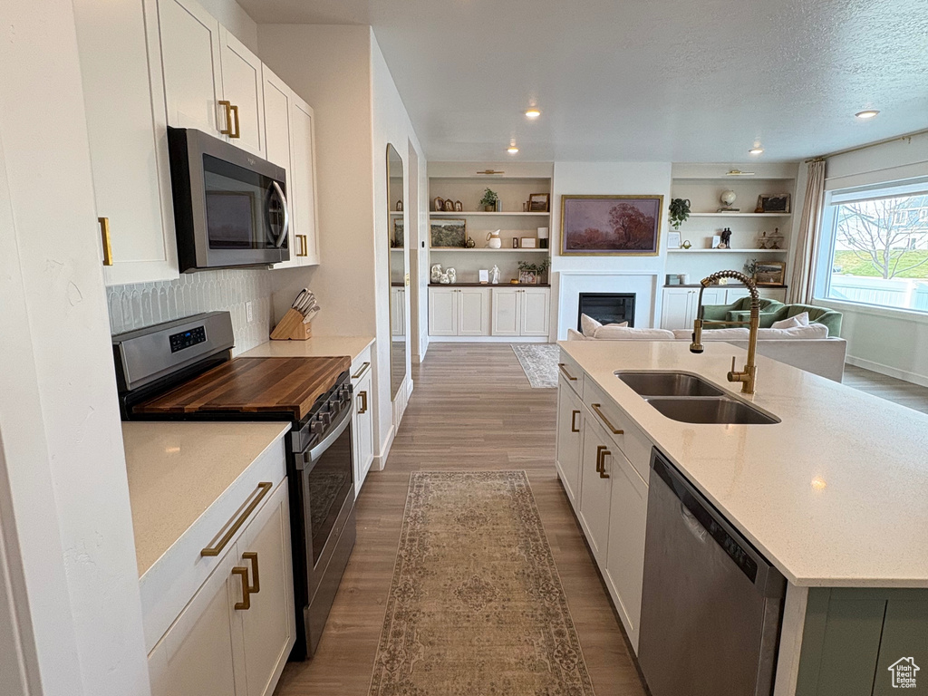 Kitchen with stainless steel appliances, a sink, open floor plan, wood finished floors, and white cabinets