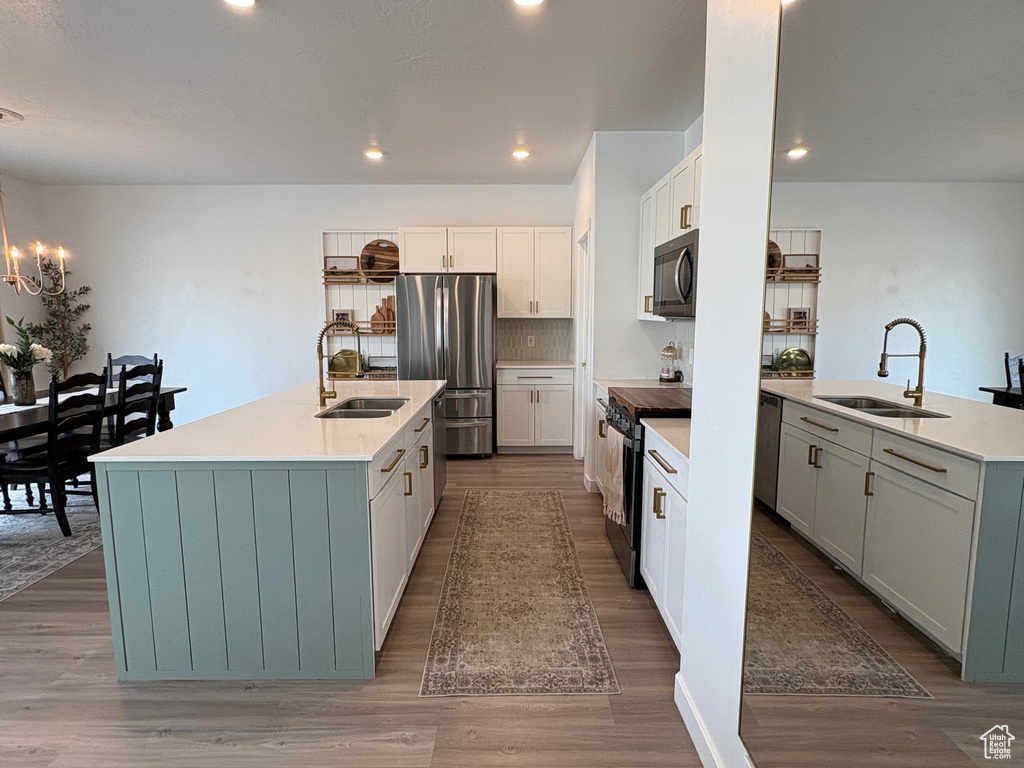 Kitchen with stainless steel appliances, a sink, an island with sink, wood finished floors, and recessed lighting