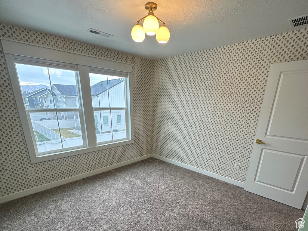 Carpeted spare room featuring a textured ceiling and wallpapered walls