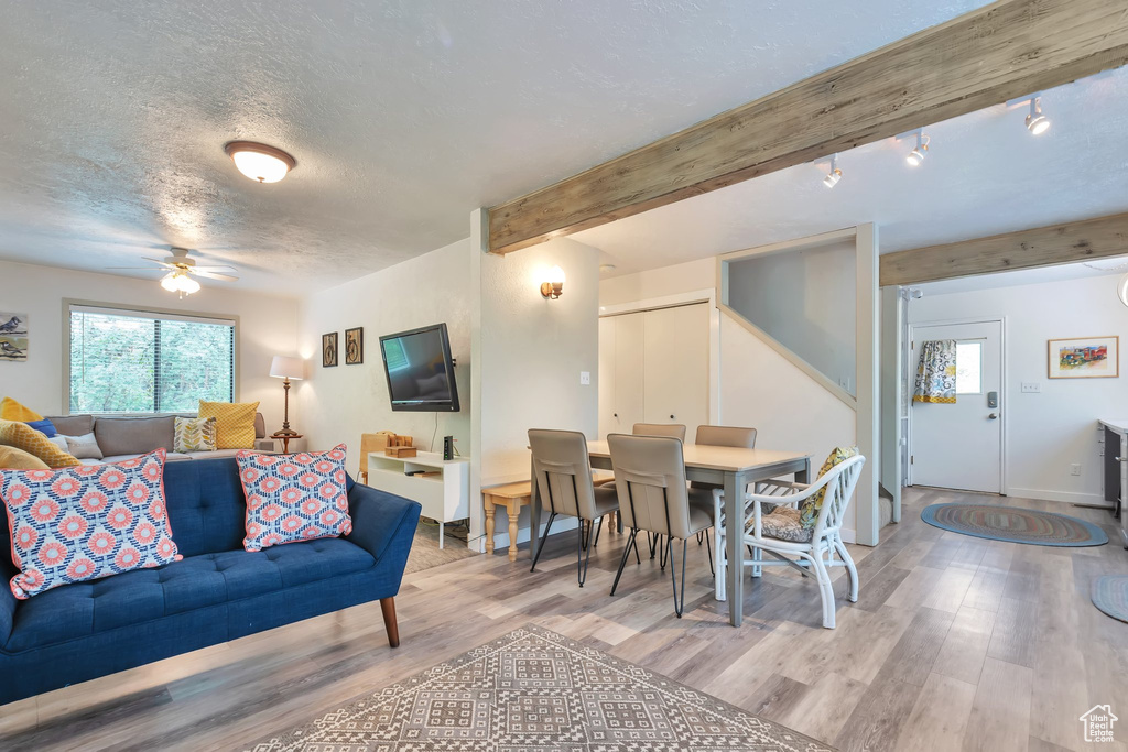 Living room featuring wood finished floors, ceiling fan, a textured ceiling, baseboards, and beamed ceiling