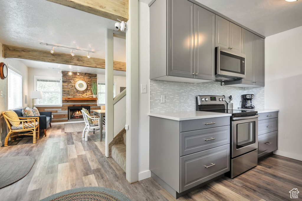 Kitchen featuring gray cabinetry, stainless steel appliances, open floor plan, wood finished floors, and backsplash