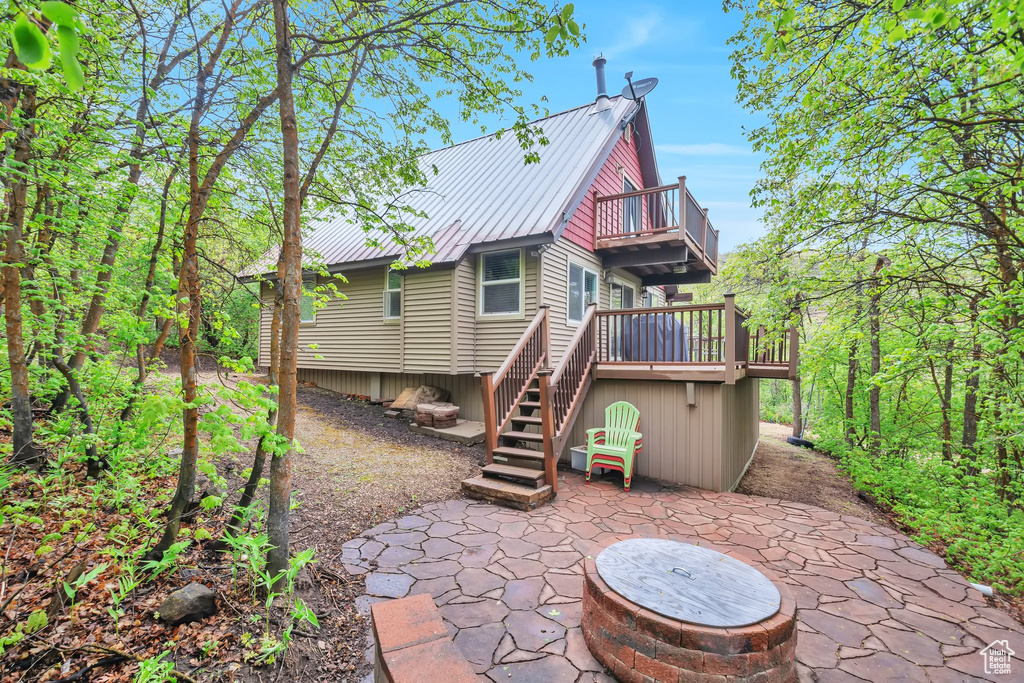 Back of property featuring a patio, a balcony, stairs, metal roof, and a wooden deck