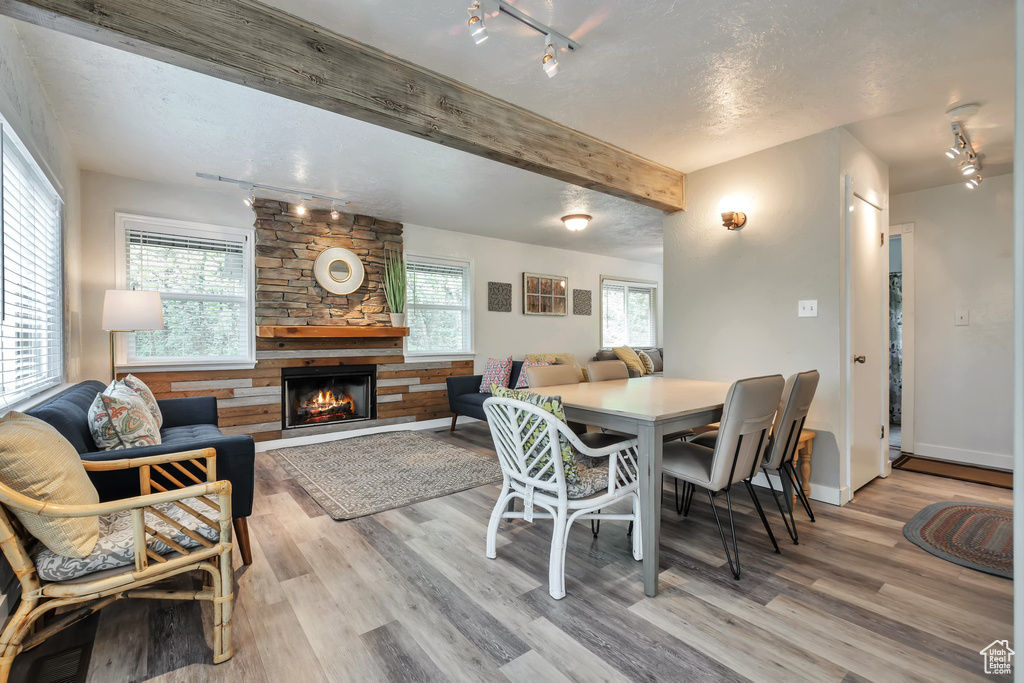 Dining room with rail lighting, a stone fireplace, light wood-style flooring, beamed ceiling, and baseboards