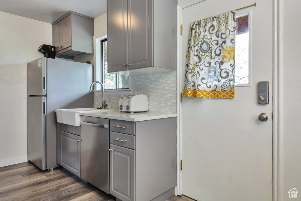 Kitchen featuring gray cabinets, stainless steel appliances, a sink, backsplash, and light countertops