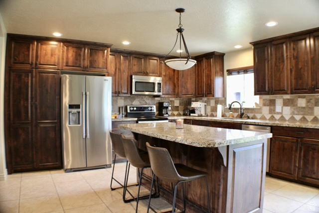 Kitchen with stainless steel appliances, a kitchen island, decorative backsplash, light stone counters, and recessed lighting