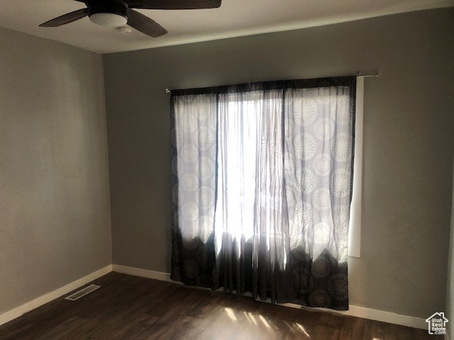 Empty room with dark wood finished floors, baseboards, and a ceiling fan