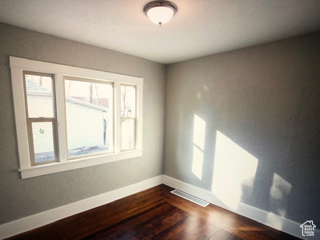 Empty room with dark wood-style floors, baseboards, and a textured wall