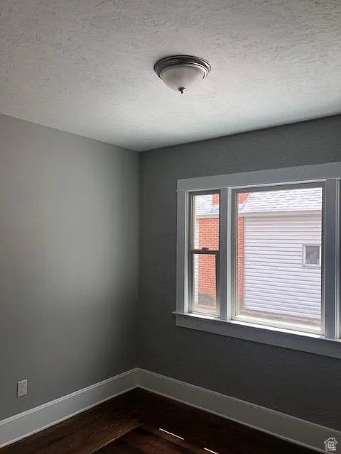 Empty room with baseboards, dark wood-type flooring, and a textured ceiling