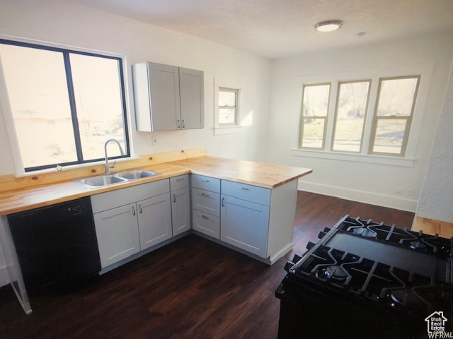 Kitchen with butcher block counters, a sink, a peninsula, dark wood-type flooring, and black appliances