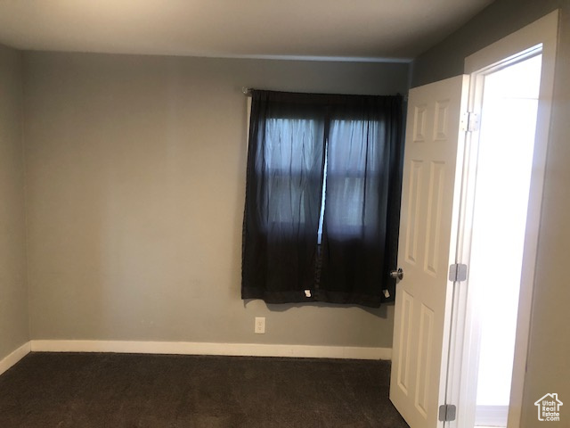 Spare room with baseboards and dark carpet