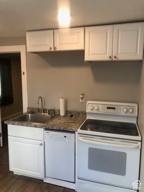 Kitchen featuring white appliances, a sink, dark wood-style floors, white cabinetry, and dark countertops