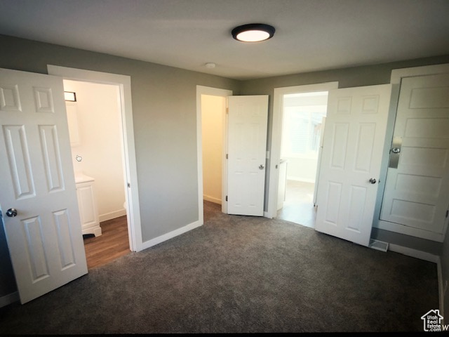 Unfurnished bedroom featuring dark carpet, baseboards, and ensuite bath