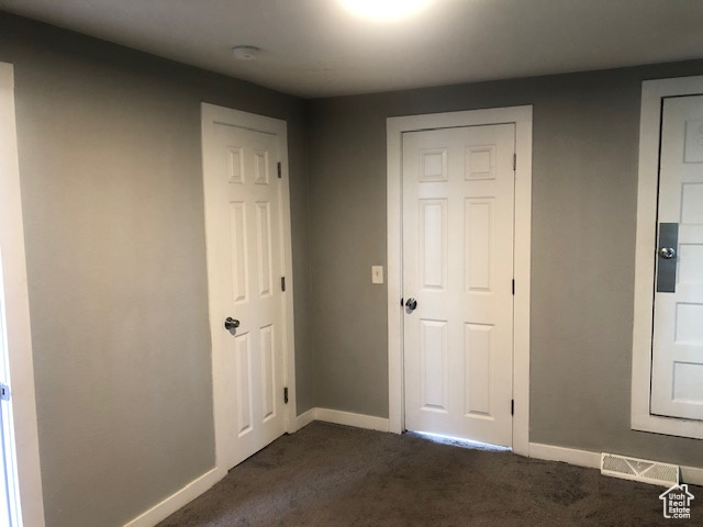 Unfurnished bedroom with dark carpet and baseboards