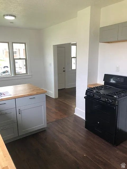 Kitchen with black range with gas cooktop, butcher block counters, dark wood-style floors, baseboards, and gray cabinetry