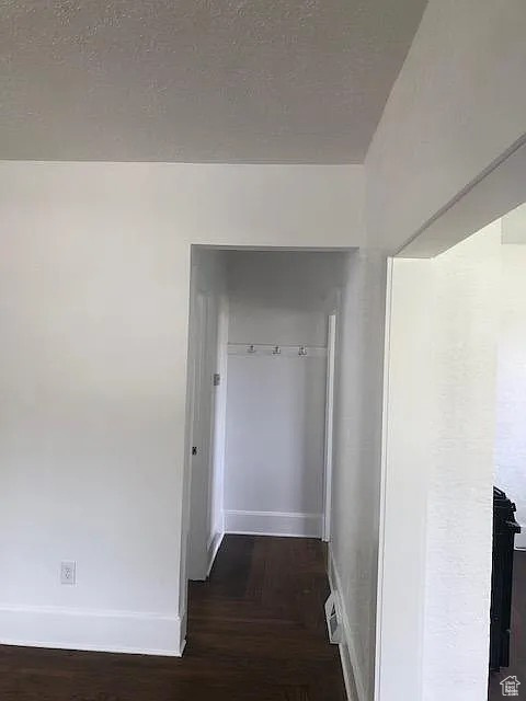 Hall with baseboards, wood finished floors, and a textured ceiling