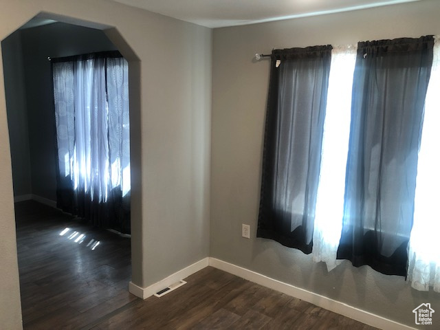 Unfurnished room featuring dark wood-style flooring, baseboards, healthy amount of natural light, and arched walkways