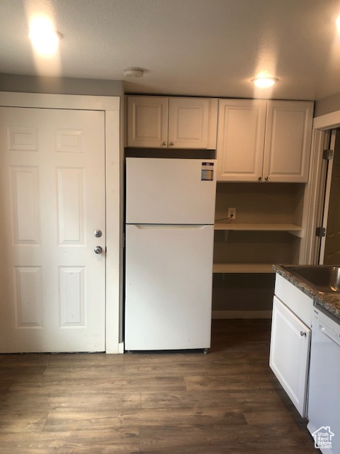 Kitchen featuring white appliances, white cabinets, dark countertops, and dark wood-style floors
