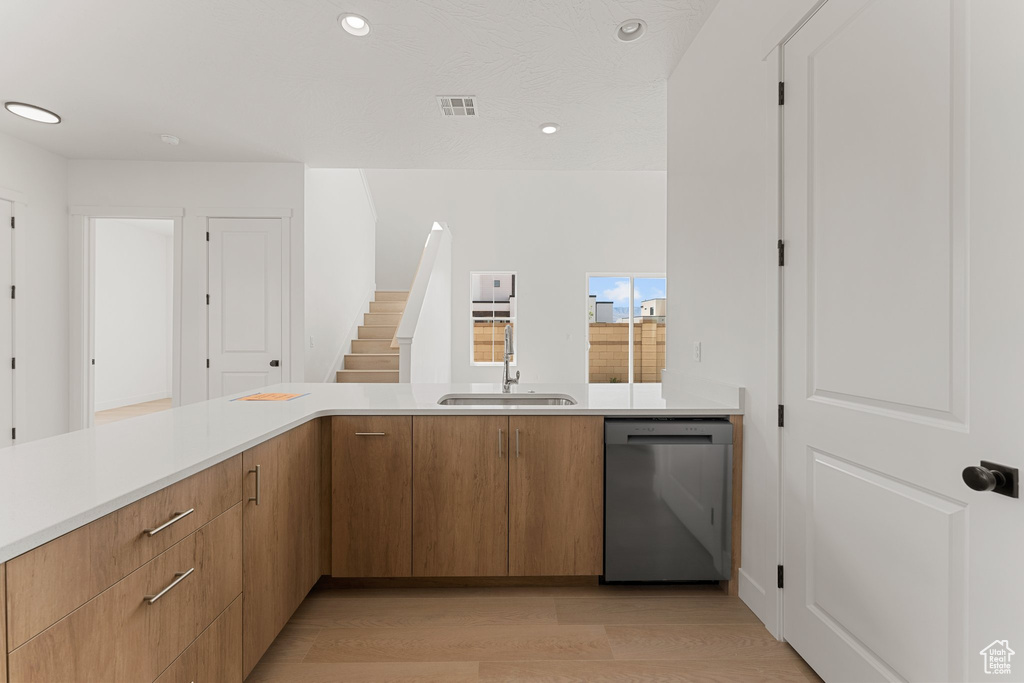 Kitchen featuring stainless steel dishwasher, a sink, light countertops, light wood-style flooring, and recessed lighting