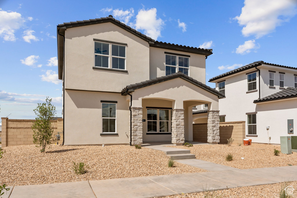 View of front of house with a tiled roof, stucco siding, fence, and stone siding