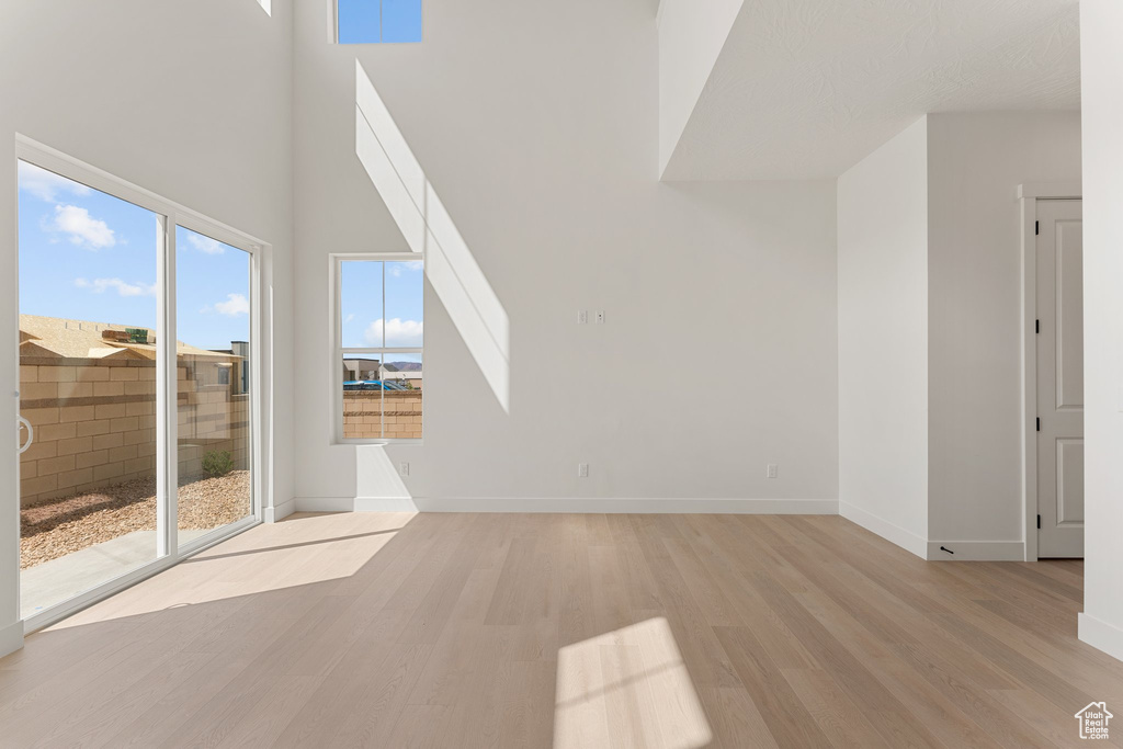 Unfurnished living room with light wood finished floors, a high ceiling, and baseboards